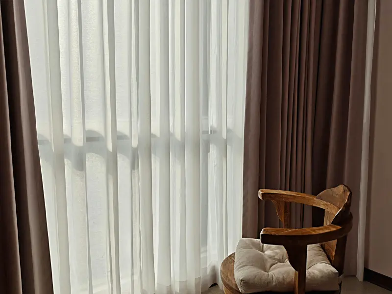 a room with window covered with curtain and a chair